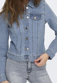 Vaaleansininen farkkutakki, jossa on muodikkaat leikkaukset, hopeiset napit, rintatasku ja saumaratkaisut. Yhdistetty harmaisiin farkkuihin.