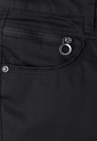 Gros plan sur un tissu noir montrant une poche zippée avec une tirette métallique circulaire et des coutures sur un vêtement.