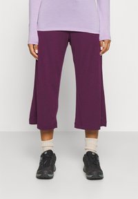 Lila korta byxor gjorda av ett mjukt tyg, med en avslappnad passform och en nederkant som når mitt på vaden, tillsammans med svarta sneakers och beige strumpor.