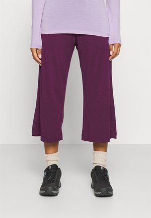 Pantalones cortos morados hechos de una tela suave, con un corte relajado y un dobladillo que llega a la mitad de la pantorrilla, combinados con zapatillas negras y calcetas beige.