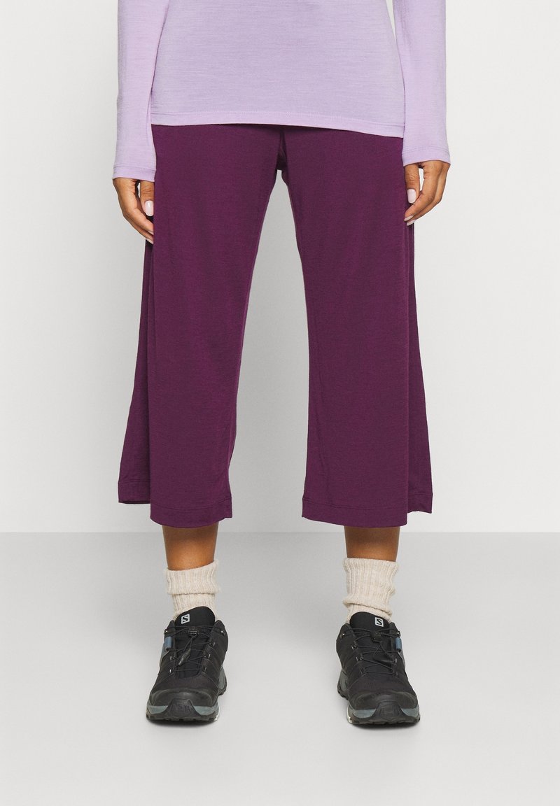 Lila korta byxor gjorda av ett mjukt tyg, med en avslappnad passform och en nederkant som når mitt på vaden, tillsammans med svarta sneakers och beige strumpor.