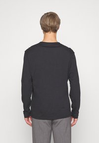 Langärmliges schwarzes T-Shirt mit Rundhalsausschnitt, aus weichem Stoff gefertigt. Es hat einen geraden Schnitt und kontrastierende Nähte an den Schultern.