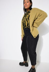 Pletený hořčicový cardigan, černé pruhované tričko, černé džíny s vysokým pasem, masivní černé boty se špunty. Hladké textury a uvolněný střih.