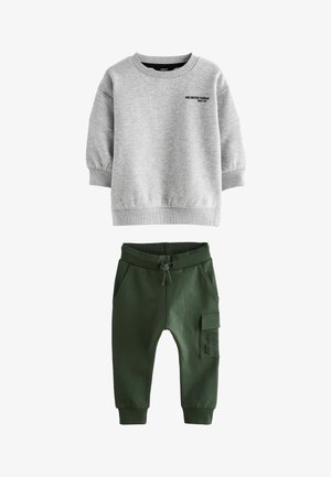 Sweatshirt gris à manches longues, avec des poignets côtelés et un texte imprimé noir. Pantalons de jogger verts avec taille élastique, poches latérales et poche cargo.