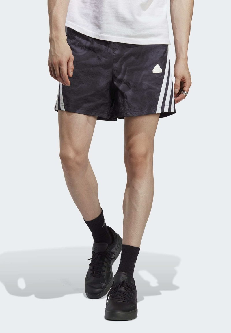 Pantaloni sportivi neri con strisce verticali bianche, realizzati in materiale leggero. Il design presenta il logo adidas sul lato sinistro.