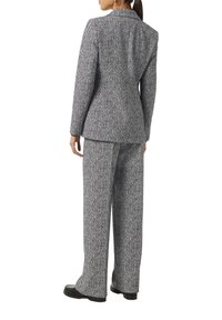 Hahnentrittmuster-Anzug in Schwarz und Weiß, bestehend aus einem strukturierten Blazer und weiten Hosen, aus strukturiertem Stoff gefertigt.