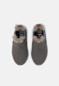 Zapatos grises tipo slip-on con una parte superior de textura suave, que cuentan con un borde gris esponjoso alrededor de la abertura y una suela de goma de color claro.
