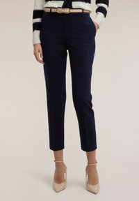 Granatowe spodnie o dopasowanym kroju, z przednimi kieszeniami i gładką fakturą. Zestawione z beżowym paskiem i cielistymi szpilkami.