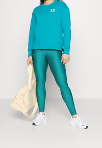 Turkusowy sweter z okrągłym dekoltem, w połączeniu z błyszczącymi tealowymi legginsami. Do tego białe sneakersy i jasnokremowa torba na siłownię.