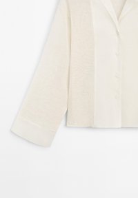 Chemise crème à manches longues, cropée, avec un tissu texturé, un col pointu et des poignets lisses contrastants.