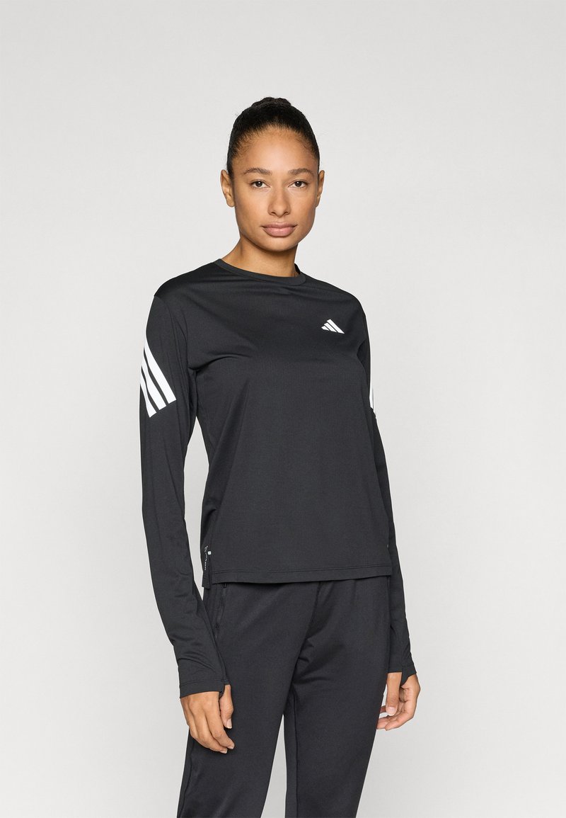 Μαύρο αθλητικό τοπ με μακριά μανίκια, λευκές τρεις ρίγες στα μανίκια και μικρό λογότυπο στο μπροστινό μέρος. Το υλικό φαίνεται λείο και εφαρμοστό.