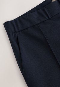 Dunkel marineblaue Hose mit elastischem Bund und vorderer Nahtdetailierung auf hellem Hintergrund.