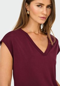 Camiseta burdeos con cuello en V, mangas cortas y una textura suave. Presenta un diseño limpio con un acabado liso.