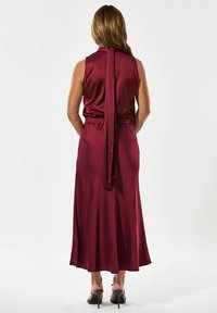 Bordo atlasas su aukštu kaklu, be rankovių dizainu ir surišimu nugaros pusėje. Turi elastingą juosmenį ir siekia vidurinį blauzdos ilgį.