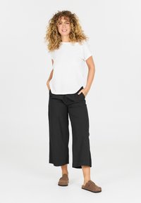 Vit kortärmad topp i kombination med lösa svarta culotte-byxor och bruna slip-on skor. Rent design med avslappnad passform och enkla färger.