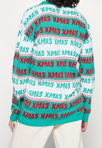 Dzianinowy sweter z motywem świątecznym, na którym widnieje napis "XMAS" w turkusowym, czerwonym i białym kolorze. Klasyczny okrągły dekolt i długie rękawy, luźny krój.