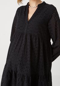 Vestido negro con mangas largas, escote en V y diseño en capas. Fabricado en tela bordada con cortes circulares; texturizado y ligero.