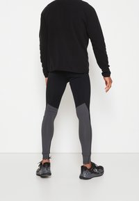 Maglietta nera a maniche lunghe abbinata a leggings aderenti con pannelli neri e grigi e scarpe da ginnastica nere con dettagli testurizzati.