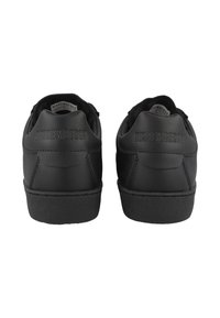 Svarta sneakers med en slät läderfinish, som har en texturerad gummisula, präglad varumärkning på hälen och en enkel design.