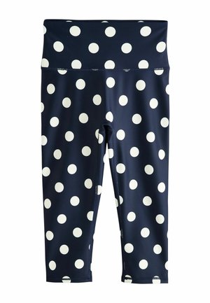 Nahaufnahme des Mittelbereichs mit marineblauen Leggings und einem passenden Croptop mit großen weißen Punkten auf glattem Stoff.