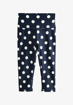 Detail stredu tela oblečený v námornícky modrých legínach a zodpovedajúcom krátkom topu s veľkými bielymi bodkami na hladkej látke.