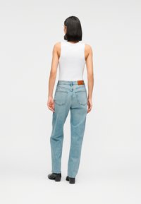 Ανοιχτό μπλε τζιν τζιν με χαλαρή εφαρμογή, ψηλή μέση και λεπτομέρειες πίσω τσέπης. Φοριέται με εφαρμοστή λευκή αμάνικη μπλούζα και μαύρα παπούτσια.