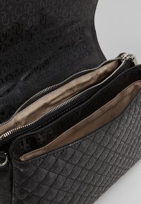 Borse nera con un esterno testurizzato con motivo a logo, due scomparti con zip foderati in velluto beige e dettagli trapuntati.