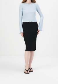 T-shirt à manches longues bleu clair à côtes avec un ourlet festonné, associé à une jupe midi noire à côtes avec une fente sur le côté, portée avec des tongs noires.