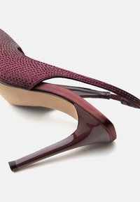 Βαθύ βουργουνδί γυναικείο παπούτσι με ψηλό τακούνι και λουράκι στην πλάτη, διακοσμημένο με στρας και με γυαλιστερό, στενό τακούνι, πάνω σε λευκό φόντο.