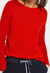 Roter strukturierten Pullover mit langen Ärmeln und Rundhalsausschnitt, kombiniert mit marineblauen Hosen mit weißen vertikalen Streifen und Kordelzugdetails.
