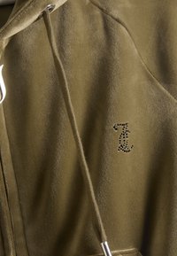 Puha anyagból készült olívazöld kapucnis pulóver, cipzáros záródással, húzózsinórral és fekete strasszköves logóval a mellrészen.