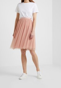 Gonna midi in tulle rosa con pois, vita arricciata, design a strati, abbinata a una t-shirt bianca e sneakers bianche.