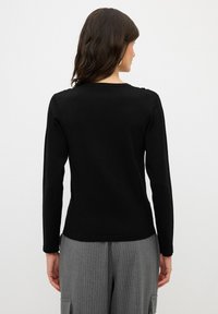 Top lungo nero a maniche lunghe con scollatura rotonda e texture liscia, abbinato a pantaloni grigi a righe sottili, che mostrano un design semplice e aderente.
