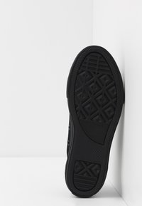 Suola di sneaker nera in gomma con un motivo di battistrada testurizzato, caratterizzata da forme a diamante in rilievo e logo del marchio. Vista laterale su sfondo bianco.