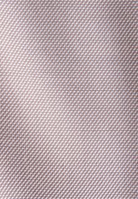 Gros plan d’un tissu texturé avec un motif diagonal répétitif de petites formes en zigzag en relief dans des tons brun clair et beige.