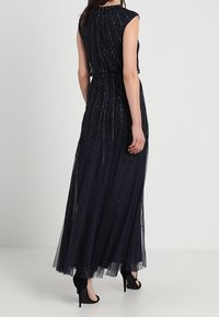 Vestido maxi azul marino con mangas cortas, que presenta un diseño de cuentas y una falda de tul fluida. Llevado con sandalias negras de tacón alto.