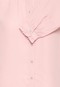 Pink long-sleeve blouse with ruffled cuffs, featuring pearly buttons along the front, and smooth, lightweight fabric texture.
