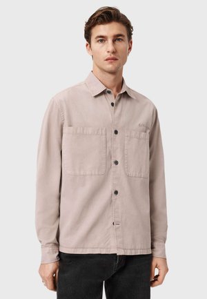 Hellbeiges Hemd aus Baumwolle mit Knöpfen, zwei Brusttaschen, schwarzen Knöpfen, langen Ärmeln und einem dezenten Logo auf der Brust.