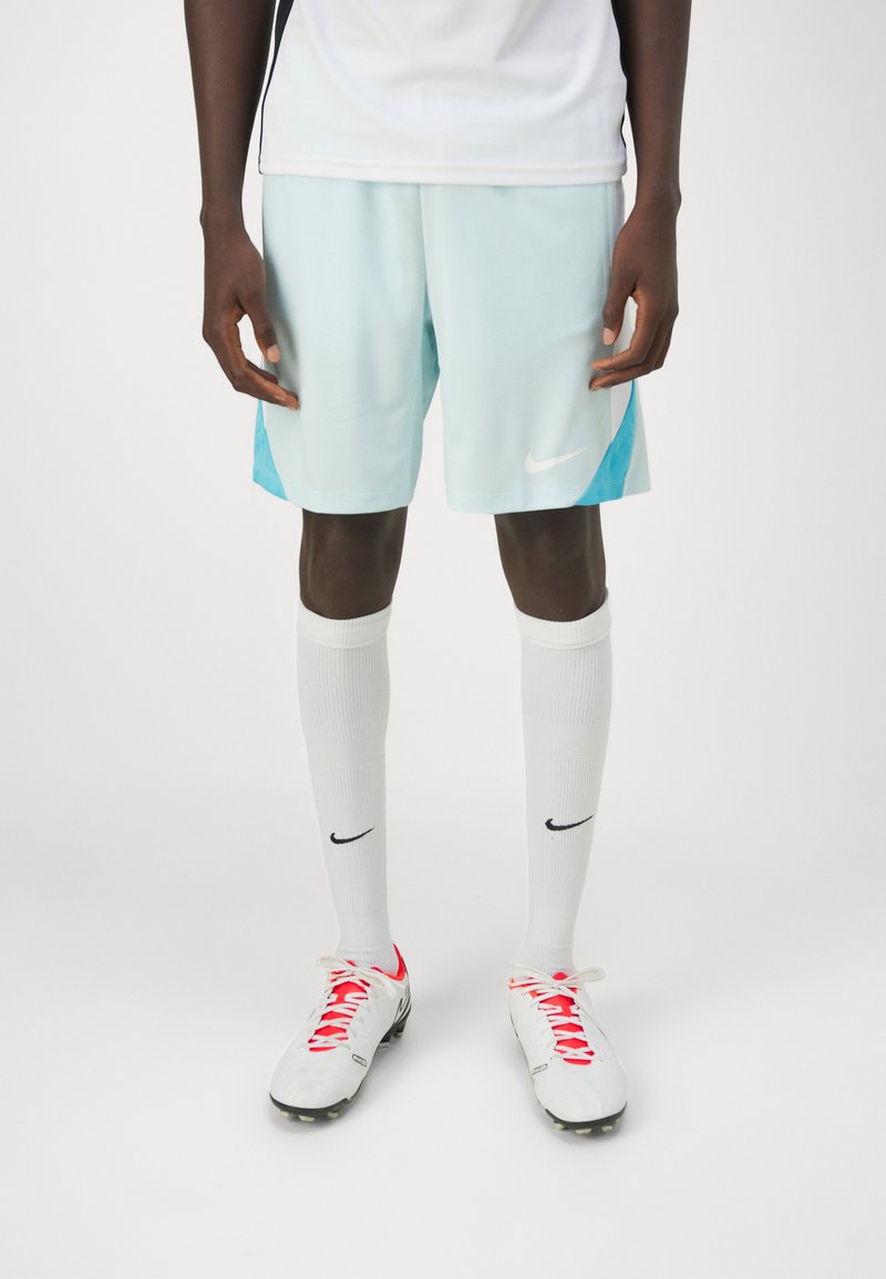 Pantalones cortos deportivos de color azul claro con un acento azul más oscuro, calcetas blancas hasta la rodilla y botas de fútbol blancas con cordones rojos y detalles negros.