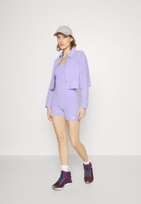Conjunto desportivo lavanda com um macacão ajustado e uma jaqueta curta com botões. Ténis de cor burdeos escuro com accents em verde-água.