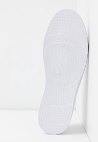 Semelle en caoutchouc blanc à motif texturé et grips circulaires, avec un logo central. Design épuré avec bords lisses et sans marques visibles.