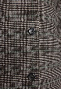 Tessuto a motivo houndstooth nero e beige con linee a griglia verdi, dotato di due bottoni neri a quattro fori.