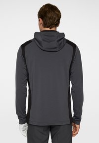 Mörkgrå sportig hoodie med en figurnära design, har svarta sidopaneler, långa ärmar och en dragsko på huvan. Lättviktig, mjuk textur.