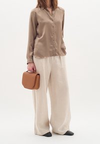 Long-sleeve, beige satin blouse with buttons, paired with wide-leg, light beige linen pants. Holding a brown leather handbag. Black flats.