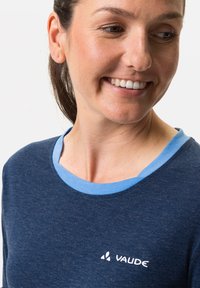 T-shirt blu navy con colletto a coste azzurro, caratterizzato da un logo bianco "Vaude" sul petto, realizzato in un tessuto testurizzato.