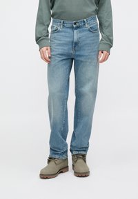 Világoskék, egyenes szabású farmernadrág denim anyagból. Ötpockets kialakítású, kifakult mosással és klasszikus gombos záródással a derékrészen.