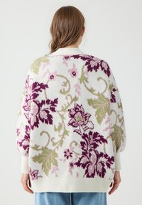 Strickpullover mit Blumenmustern in Creme, featuring lila und grüne Muster, oversized Schnitt, gerippte Bündchen und Saum. Strukturierter, gemütlicher Stoff.