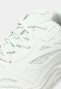 Λευκό αθλητικό παπούτσι με υφασμάτινο επάνω μέρος με υφή, επικάλυψη διακοσμητικών στοιχείων και παραδοσιακό σύστημα δέσιμου. Καμπυλωτός σχεδιασμός σόλας από καουτσούκ.