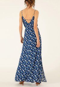Robe maxi florale bleue avec des bretelles fines, un dos en V et une silhouette fluide. Comprend des motifs floraux blancs et bleu clair.
