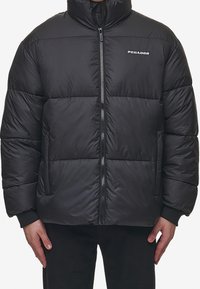 Giubbotto imbottito nero con colletto alto, chiusura con zip frontale e logo sul petto. Morbido, con texture trapuntata, presenta polsini elasticizzati e tasche laterali.